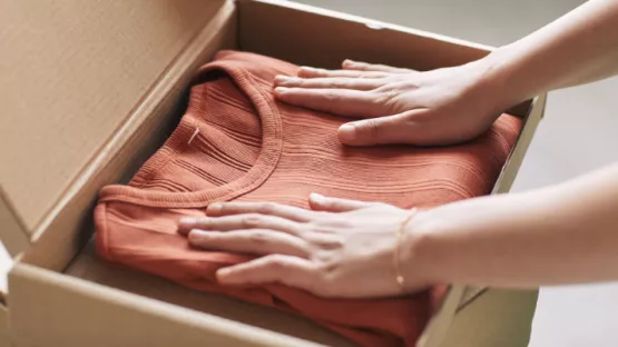 Mani che mettono vestiti all'interno di uno scatolone