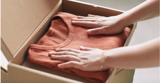 Mani che mettono vestiti all'interno di uno scatolone